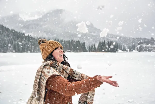 一个戴着舒适的冬季围巾和帽子的女人在荒野里与雪玩耍 开心地笑着 — 图库照片