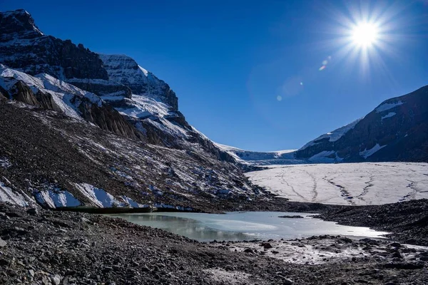 겨울에 눈덮인 산비탈 기슭에 얼어붙은 호수가 이비치는 — 스톡 사진
