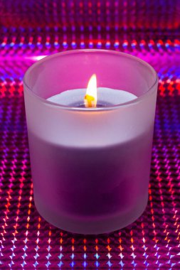 Canlı ve soyut bir arkaplanda, yanan bir mumun bardaktaki dikey yakın çekimi.