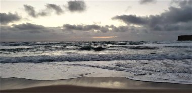 Bulutlu bir günde okyanusun kumlu sahiline köpüklü dalgaların panoramik görüntüsü.