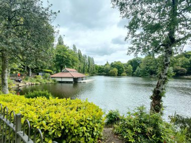 Büyük yeşil ağaçlarla çevrili küçük gölü olan güzel bir park.