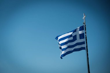 Yunanistan bayrağı açık mavi gökyüzüne karşı bayrak direğinde dalgalanıyor.
