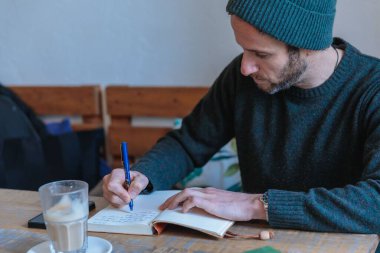 Not defterine tahta masada kahve yazan genç bir adam.