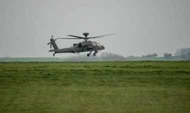 Koyu gri bir ordu saldırı helikopteri gündüz uçuyor.