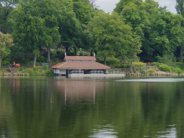 Büyük yeşil ağaçlarla çevrili küçük gölü olan güzel bir park.