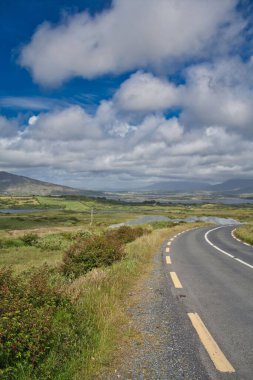Bulutlu gökyüzünün altında bir dağ yolunun güzel dikey görüntüsü.