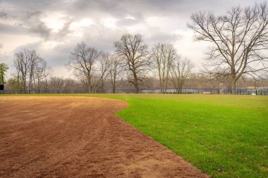 Tarifsiz lise softball sahasının birinci kaleden ikinci kaleye doğru kil saha içi bakışıyla görüntüsü. Görünürde kimse yok.