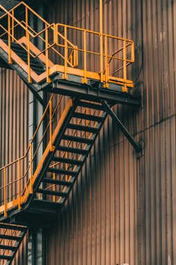 Gündüz vakti paslı turuncu duvarı ve merdivenleri olan bir yapının dikey görüntüsü.