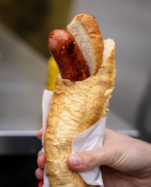 Sosisli sandviç tutan bir elin dikey çekimi, sosis dolu bir sandviç ve bir parça ekmek.