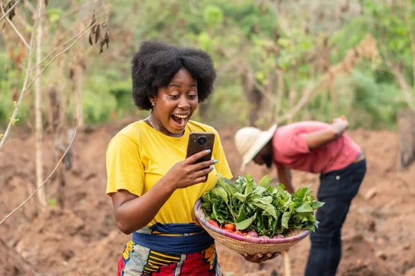 Heyecanlı kadın Afrikalı çiftçi telefonunu kontrol ediyor.