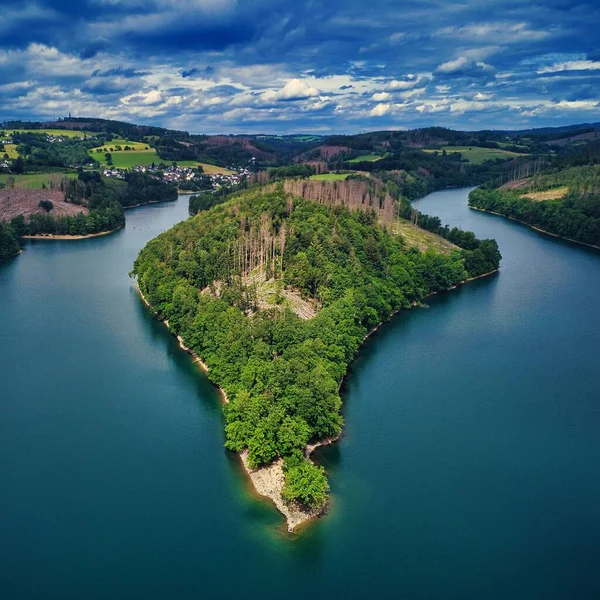 stock image A drone view of hills and fields covered in greenery surrounded by the water on a cloudy day