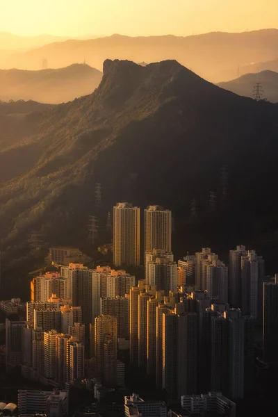日没時に山の背景に背の高い高層ビルの垂直ショット — ストック写真