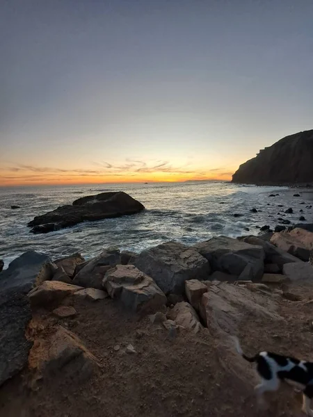 在落日的橙色天空下 一个岩石的海滩 岩石喷涌而出的大海 垂直的射击 — 图库照片