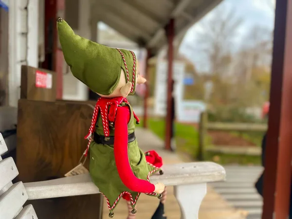 Photo of a small holiday Elf sitting on the arm of an outside bench.