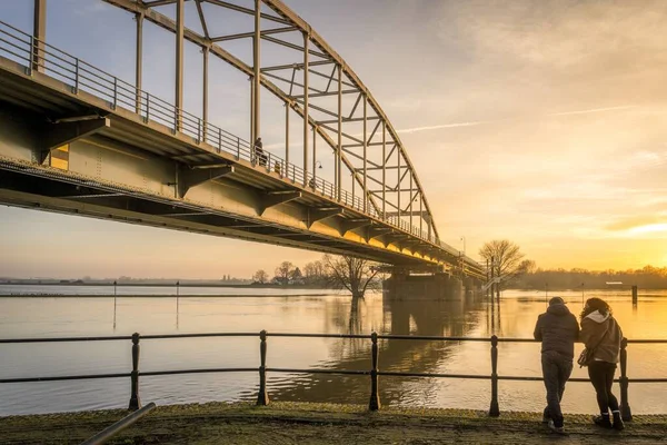 Två Damer Tittar Bro Över Lugn Flod Solnedgången — Stockfoto