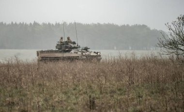 Bir askeri tank ve tarlada silahlı askerler.