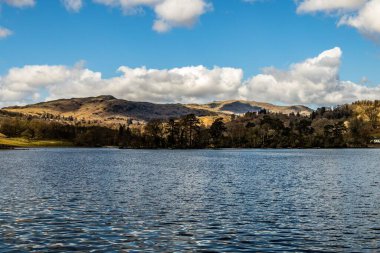 Dağların ve vadilerin manzaralı görüntüsü bulutlu bir gökyüzünün altında bir göl boyunca.