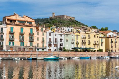 Bosa, Sardinya 'daki bir tepenin arkasında bir şato olan gölün kıyısındaki antik renkli bir binanın manzarası.