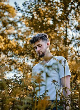 Kafkasyalı bir adamın dikey görüntüsü. Kafası aşağıda. Ormandaki çalıların arasından görülüyor.