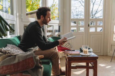 Kafkasyalı adamın kanepede oturup kitap okuduğu dikey bir fotoğraf.