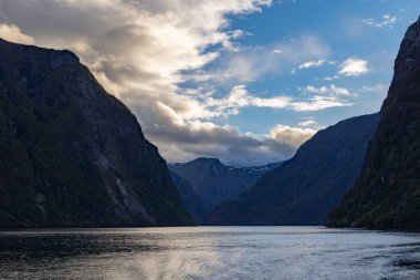 Gökyüzü arka planında gölle çevrili devasa kayalık dağların manzarası.
