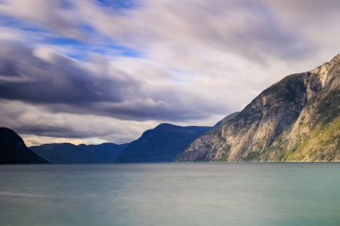Bulutlu bir gökyüzünün altında dağlarla çevrili güzel bir göl görüntüsü.