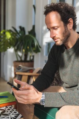 Kafkasyalı adamın kanepede oturup akıllı telefona baktığı dikey bir fotoğraf.