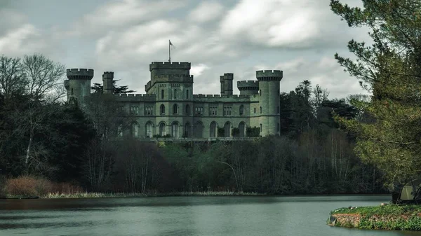 stock image The beautiful Castle of Eastnor surrounded by trees and a lake against the cloudy sky