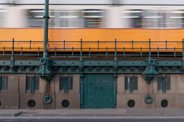헝가리 부다페스트에서는 파란색낡은 건물에서 빠르게 움직이는 주황색 열차가 장시간 노출됐다 — 스톡 사진