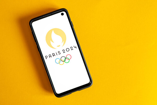 A flat lay of a phone with Paris 2024 and the Olympics logo and eternal fire on it against a yellow background