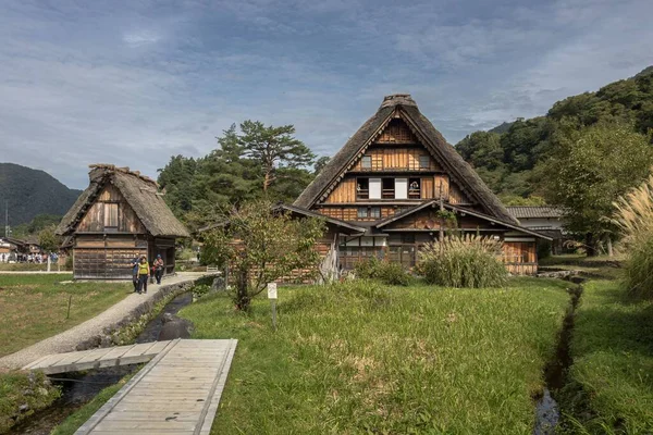 日本の白川郷や五箇山の歴史的な村を訪れ 木々に囲まれ 背景には森林に覆われた山を訪れる観光客のグループ — ストック写真