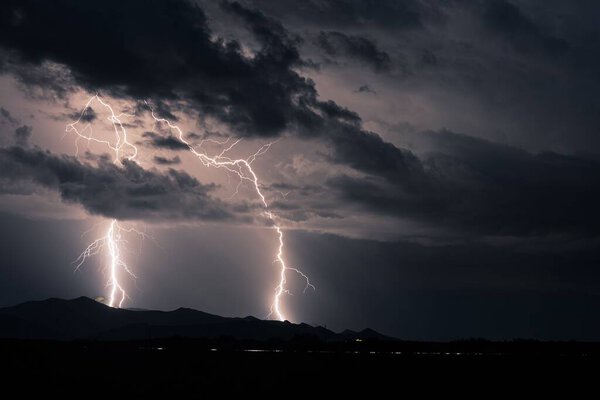 A huge storm over distant mountains with bolts of lightning flashing across the sky