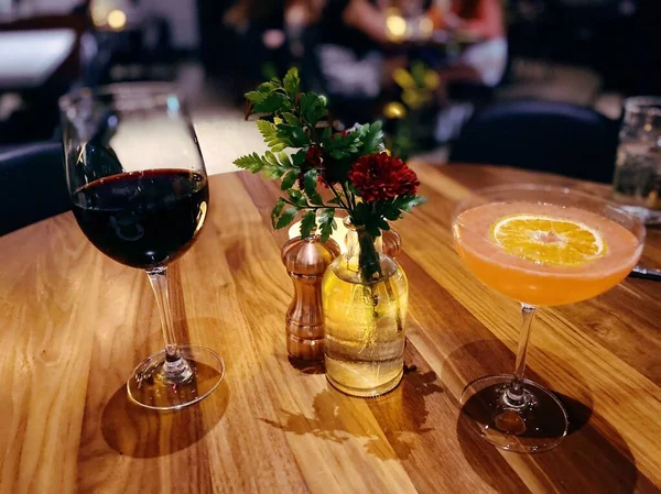 一张特写镜头 是一张木制餐桌的特写镜头 桌上放着一杯红酒和橙子鸡尾酒 — 图库照片