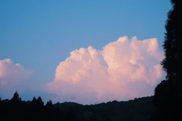 丘や木のシルエットを背景に青空に浮かぶ白いふわふわの雲の風景 — ストック写真