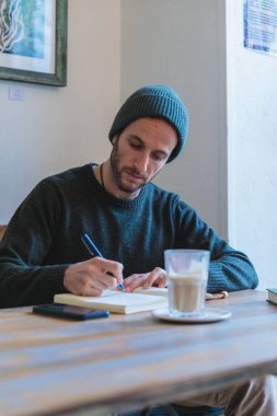 Not defterine tahta masada kahve yazan genç bir adam.