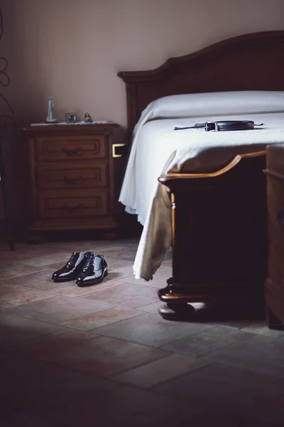床に黒い男の靴のペアとベッドの上にベルトの垂直ショット — ストック写真