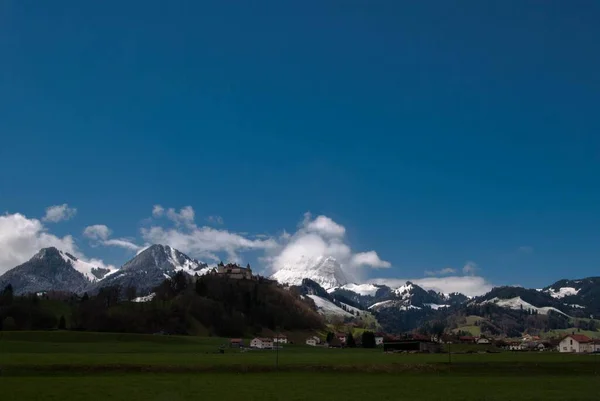 Zielony Krajobraz Domami Wiejskimi Śnieżną Górą Błękitnym Pochmurnym Niebem — Zdjęcie stockowe
