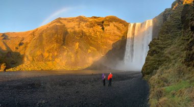 İzlanda 'daki Skogafoss şelalesinin önünde turistlerle manzaralı bir çekimi.