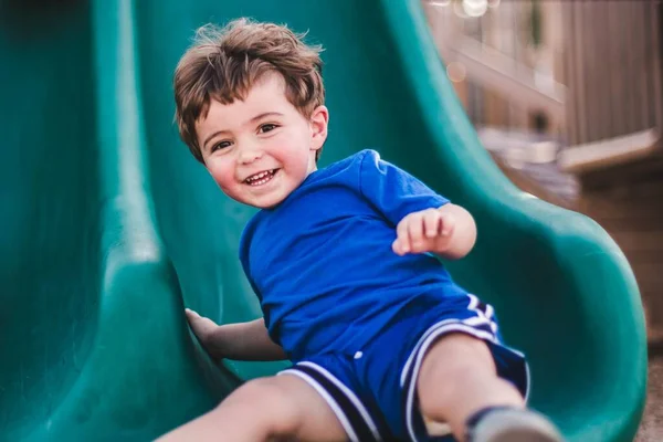 遊び場で滑りながら幸せを感じる白人の少年 — ストック写真
