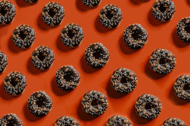 Çikolatayla kaplanmış, turuncu arka planda minik balkabağı fenerleriyle süslenmiş taze pişmiş çöreklerin üst görüntüsü.