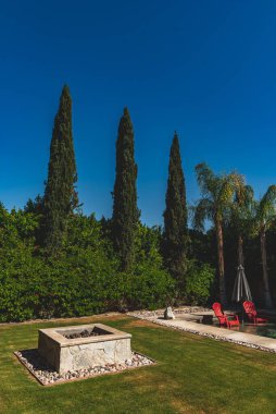 Evin arka bahçesindeki şömineli ve havuzunda kırmızı sandalyeli dikey bir fotoğraf.