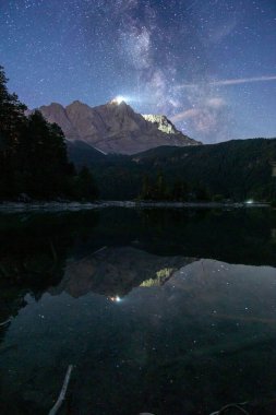 Göle yansıyan dağların ve ağaçların dikey görüntüsü yıldızlı bir gece göğü.