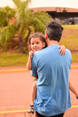 Latin bir babanın sokakta kızına sarılırken çekilmiş dikey bir fotoğrafı.