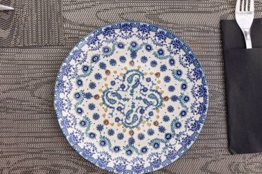 Mavi boş tabağın üst manzarası. Güzel bir çiçek süslemesi ve yakınındaki çatalla.