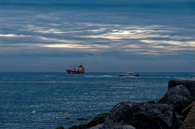 Birkaç gemi açık denizde ilerlerken alacakaranlıkta mavi gökyüzünün arka planına karşı.