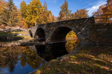 Callicoon Creek 'teki suya yansıyan taş kemer köprüsünün ve sonbahar ağaçlarının manzarası.