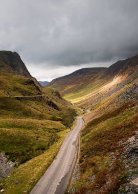 Bulutlu bir gökyüzünün altındaki dağ vadisinde bir yolun dikey görüntüsü.