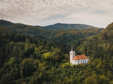 Slovenya 'nın dağlık bir bölgesinde yoğun bir ormanla çevrili bir kilise ve kule anteni.