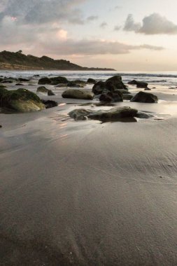 Akşamları arka planda sakin bir deniz olan kayalarla dolu bir plajın dikey çekimi.