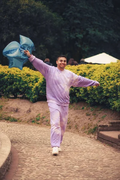 一个快乐的西班牙裔男子在公园里拿着蓝色气球散步的垂直镜头 — 图库照片